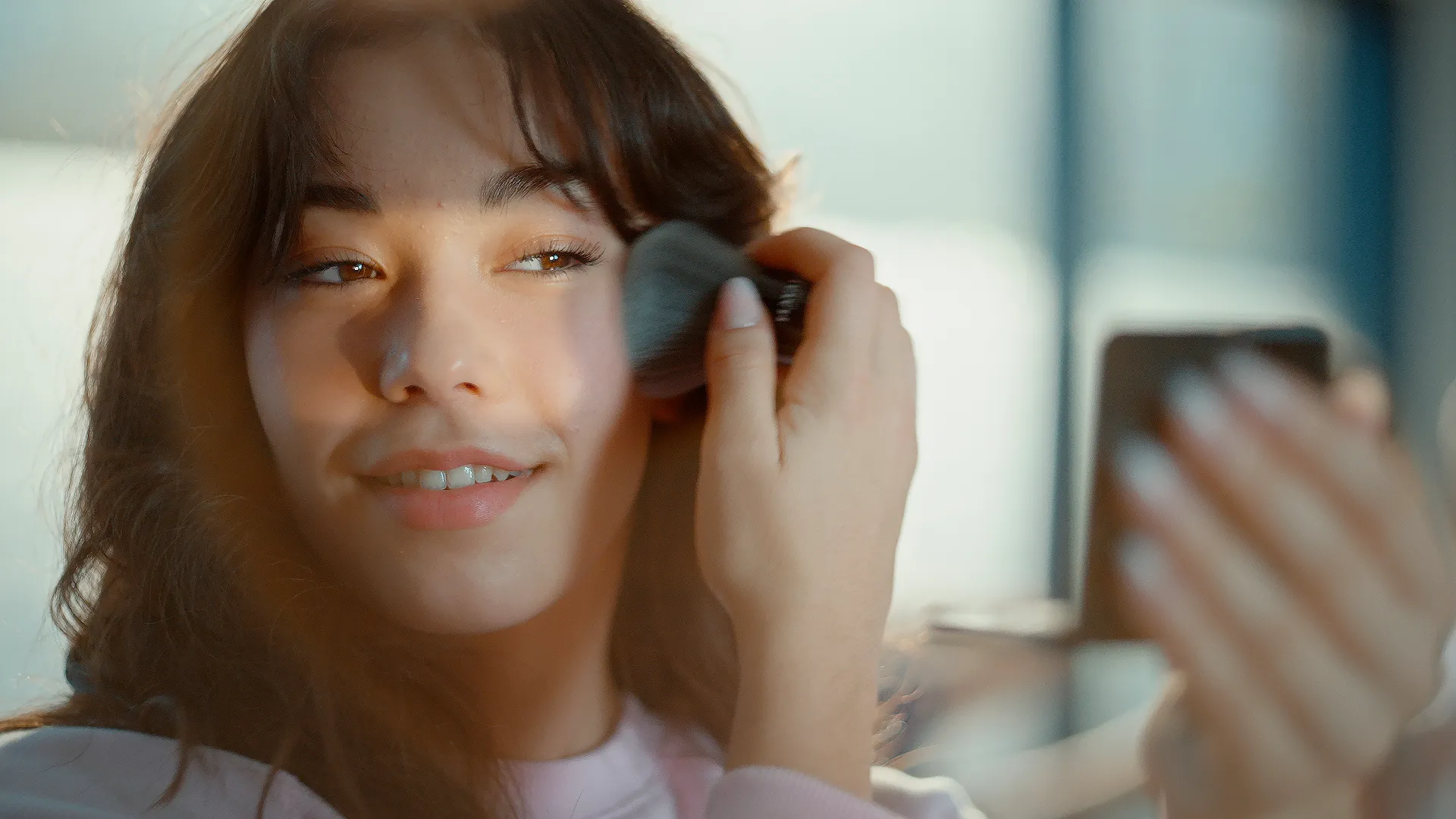 A young woman smiling while applying makeup with a brush, symbolizing self-care and beauty advice in practice.